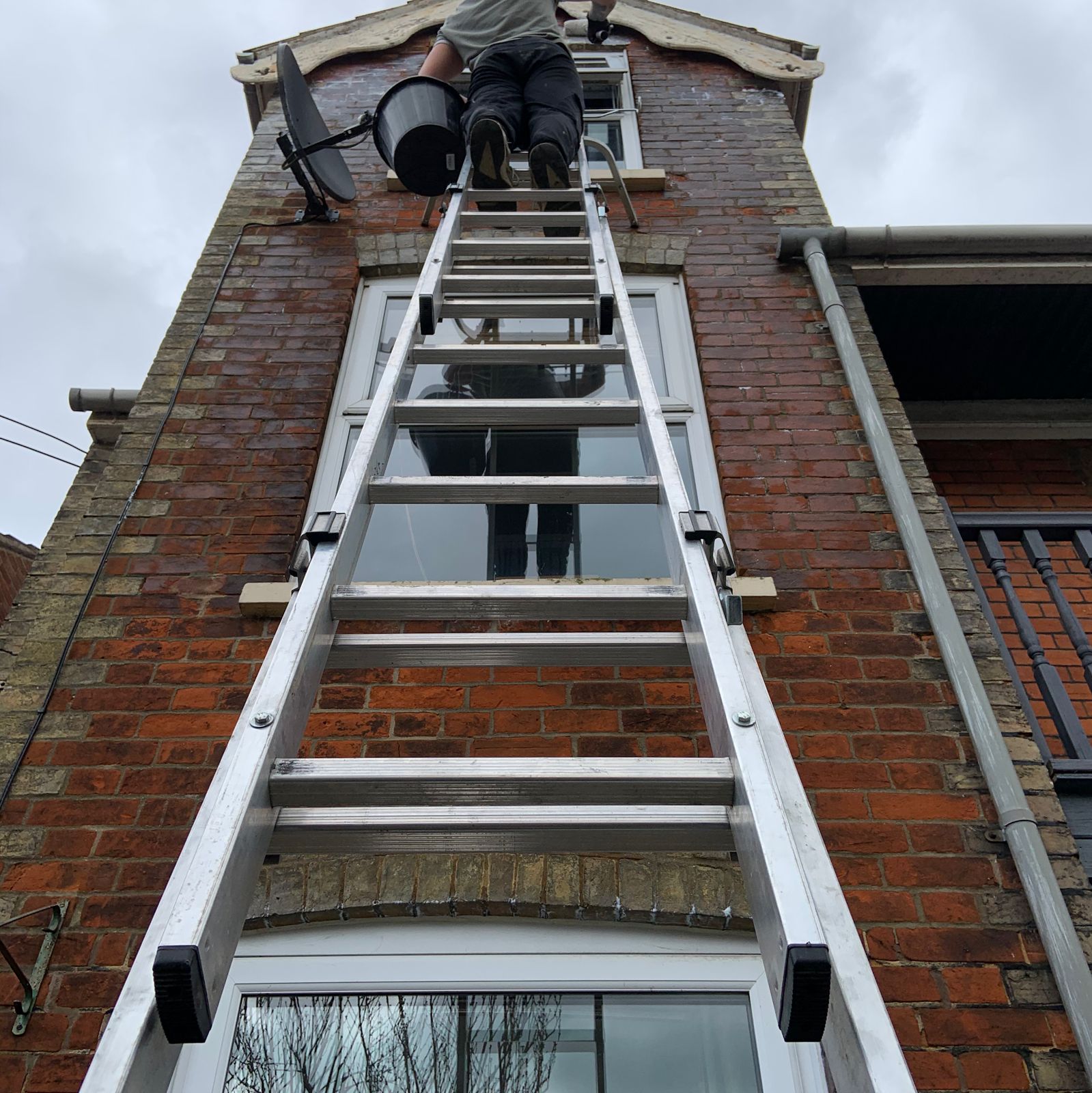Working from a ladder high up a red brick gable